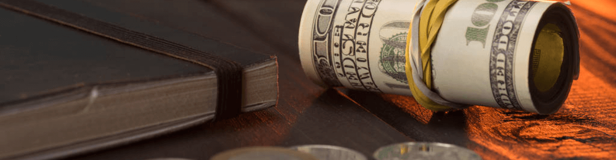 Rollo de billetes de dólares estadounidenses con monedas y libreta sobre una mesa de madera.
