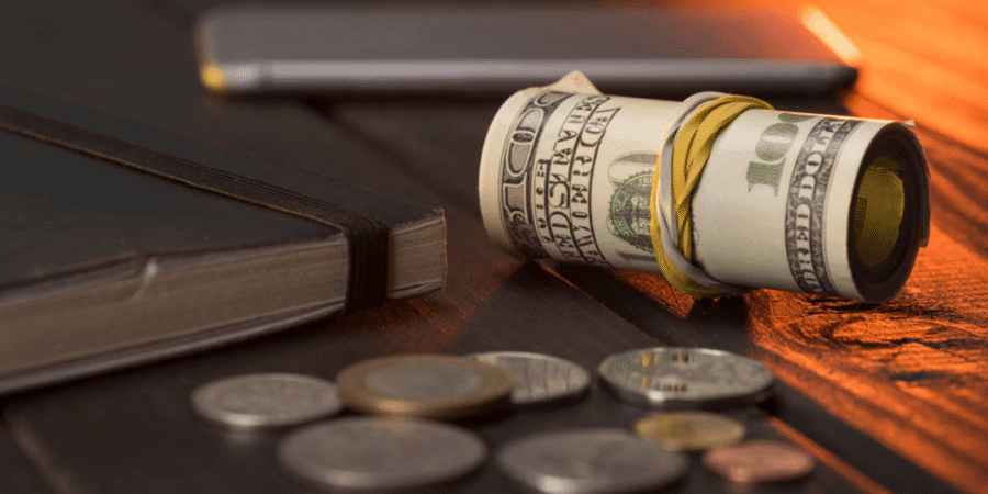 Rollo de billetes de dólares estadounidenses con monedas y libreta sobre una mesa de madera.